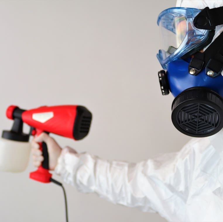 A Painter Working on Spraying a Wall With White Color